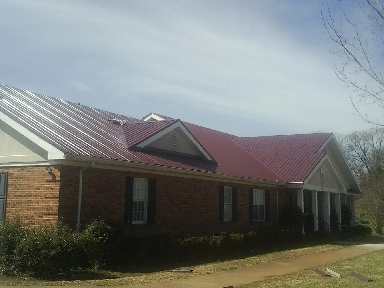 Red metal roof with gabled entries on a long brick building, from a Hail Damage Roof Repair job in Walnut